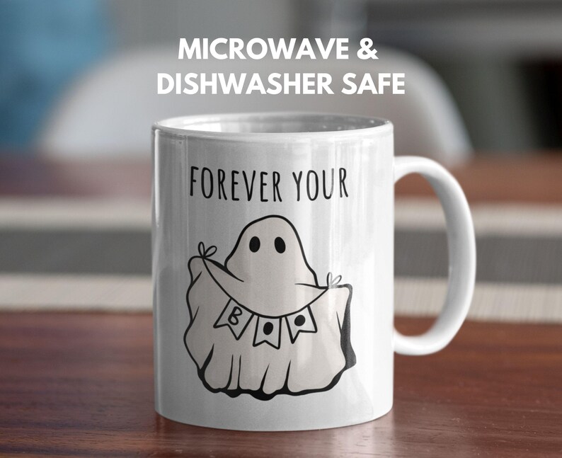 May include: White ceramic mug with a black ghost illustration holding a banner that says "BOO". The mug has the text "FOREVER YOUR" above the ghost and "MICROWAVE & DISHWASHER SAFE" above the mug. The mug has a white handle.