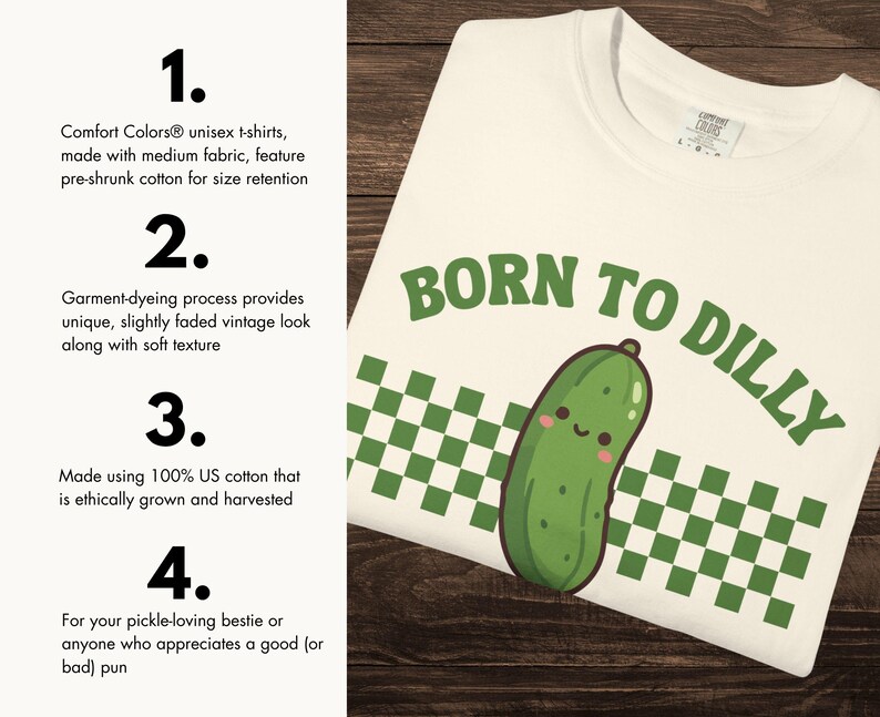 May include: Cream-coloured unisex t-shirt with the phrase "BORN TO DILLY" in green lettering, featuring a smiling cartoon pickle. The shirt has a green and white checkered pattern and is made of medium fabric.