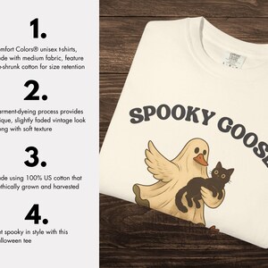 May include: A white Comfort Colors t-shirt with the words "SPOOKY GOOSE" in dark brown. The shirt features a cartoon ghost with a duck's beak and a black cat. The shirt is made of medium fabric and pre-shrunk cotton.
