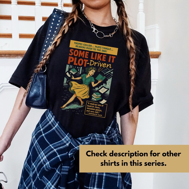 May include: Black t-shirt with a retro graphic design. The design shows a woman with books and the words "SOME LIKE IT PLOT-DRIVEN". The text also includes "TROPES COLLIDE... PLOTS TANGLE... READERS RUSH TO THE END!" and "A madcap tale of bookish chaos..."