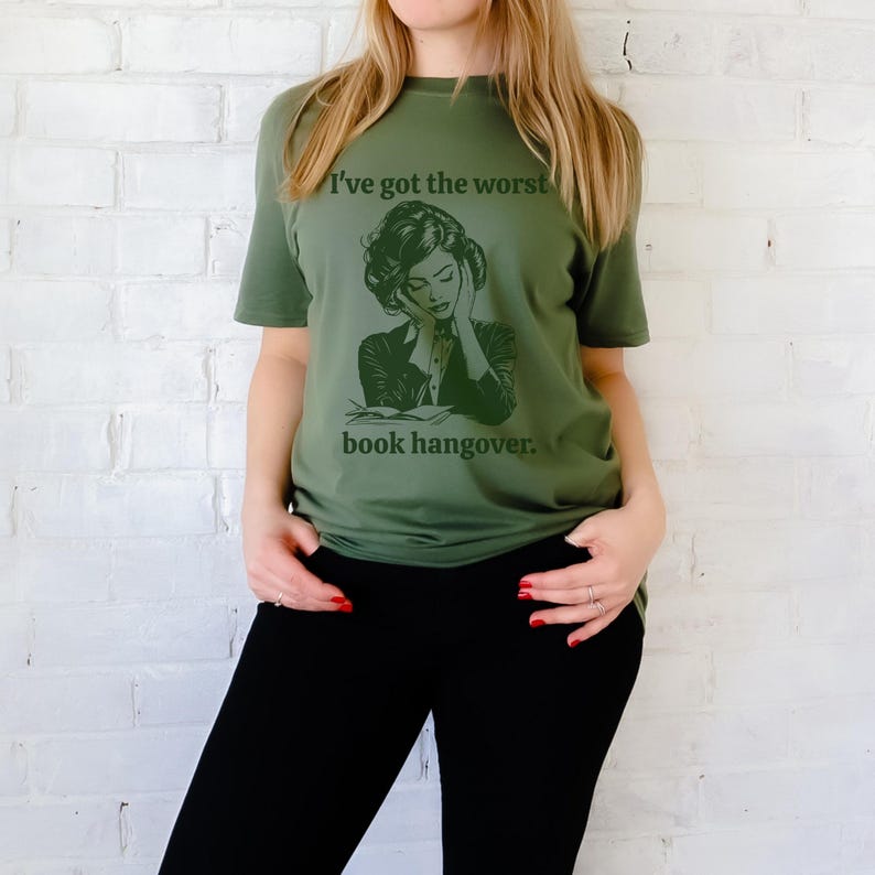 Op de afbeelding: Groen T-shirt met een afbeelding van een vrouw die een boek leest en de tekst "Ik heb de ergste kater van een boek."