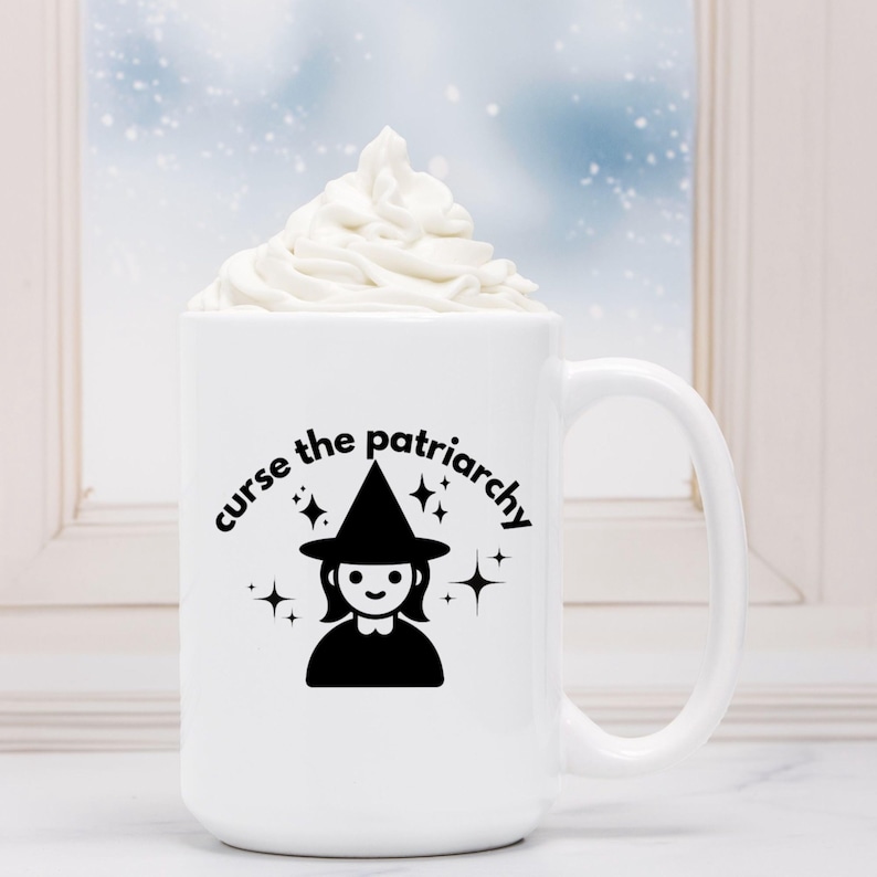 May include: White ceramic mug with a black graphic of a witch with a pointed hat and the text "curse the patriarchy". The mug has a black handle and is filled with white whipped cream.