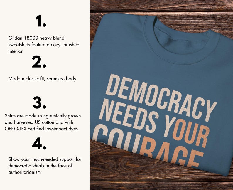 Puede incluir: Una camiseta azul con la frase "DEMOCRACY NEEDS YOUR COURAGE" en letras blancas y naranjas. La camiseta est&aacute; hecha de algod&oacute;n estadounidense cultivado y cosechado &eacute;ticamente.