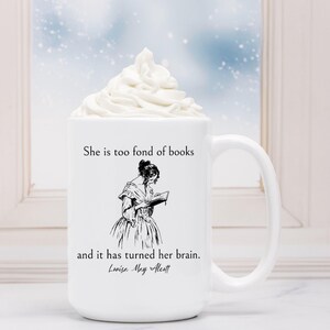May include: White ceramic mug with a black and white illustration of a woman reading a book. The mug has the text "She is too fond of books and it has turned her brain. Louisa May Alcott" printed on it.