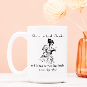 May include: White ceramic mug with a black and white illustration of a woman reading a book. The mug has the text "She is too fond of books and it has turned her brain. Louisa May Alcott" printed on it.