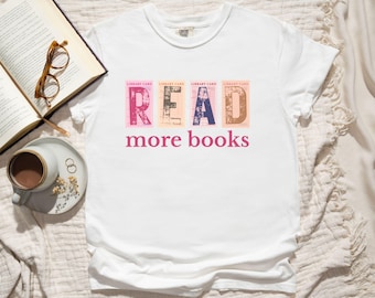 May include: White t-shirt featuring the word "READ" in colourful library card-style letters, and the words "more books" in pink. A book, glasses, and a cup of coffee are in the background.