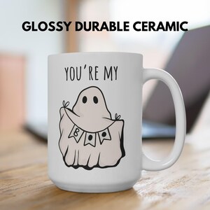May include: White ceramic mug with a black handle featuring a ghost illustration holding a banner that says "BOO". The mug has the text "YOU'RE MY" above the ghost. The mug is labeled "GLOSSY DURABLE CERAMIC".