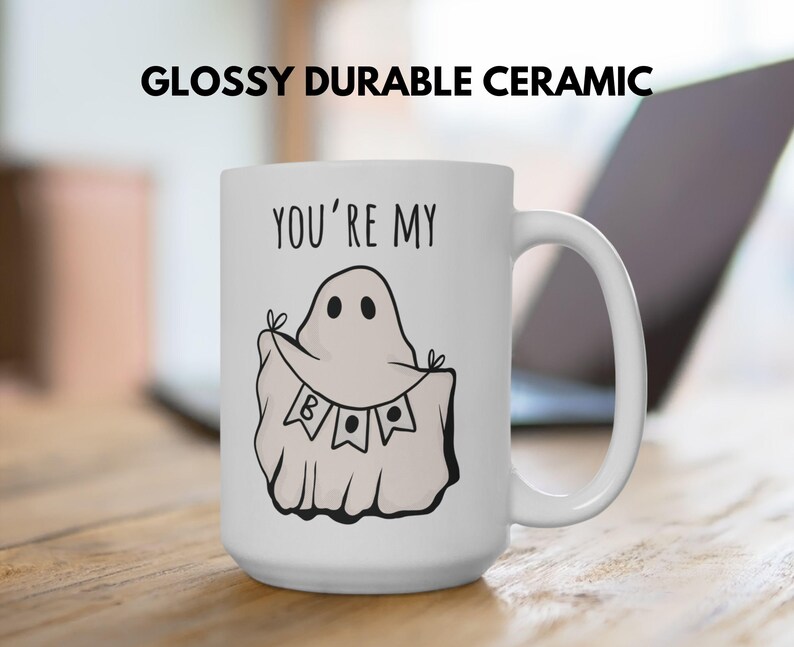 May include: White ceramic mug with a black handle featuring a ghost illustration holding a banner that says "BOO". The mug has the text "YOU'RE MY" above the ghost. The mug is labeled "GLOSSY DURABLE CERAMIC".