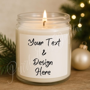 Könnte beinhalten: Eine brennende Kerze in einem transparenten Glas mit einem weißen Etikett. Auf dem Etikett steht "Your Text & Design Here" in schwarzer Schrift. Die Kerze ist von Weihnachtsdekorationen umgeben, darunter eine goldene Kugel und Tannenzweige.