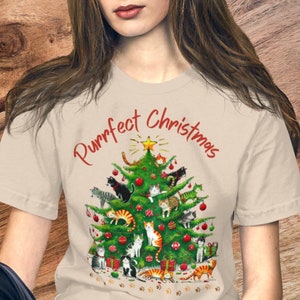 May include: A beige t-shirt with a Christmas tree design featuring a variety of cats and the text "Purrfect Christmas".