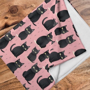 以下が含まれることがあります： ピンクのフリースブランケットに黒い猫の模様が描かれています。猫はすべて前を向いており、目は開いていて口は閉じられています。ブランケットは柔らかく、抱きしめるのに最適です。