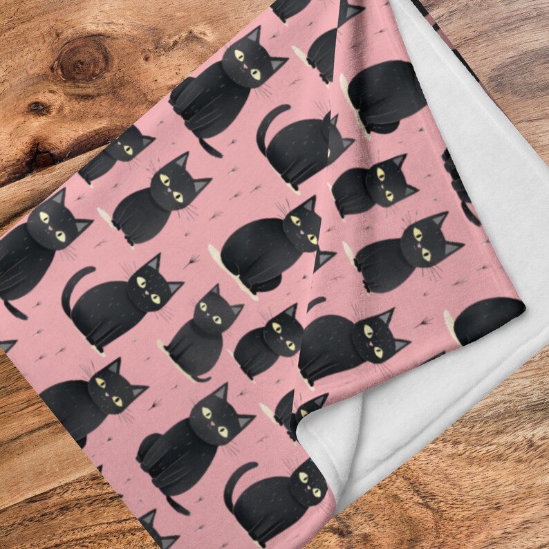以下が含まれることがあります： ピンクのフリースブランケットに黒い猫の模様が描かれています。猫はすべて前を向いており、目は開いていて口は閉じられています。ブランケットは柔らかく、抱きしめるのに最適です。