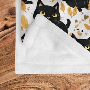 May include: White fleece blanket with a black cat and yellow leaf pattern. The blanket is folded in half and the pattern is visible on the front side.