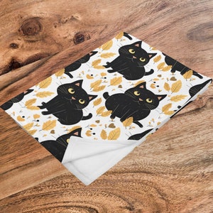 May include: White fleece blanket with a black cat and yellow leaf pattern. The cat is cartoon-like and has big eyes.