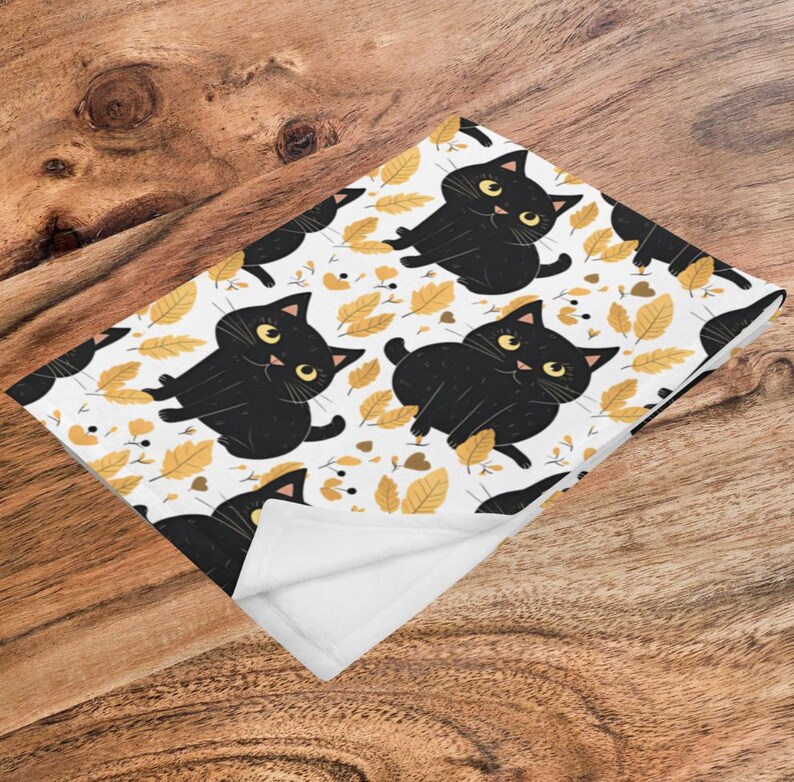 May include: White fleece blanket with a black cat and yellow leaf pattern. The cat is cartoon-like and has big eyes.