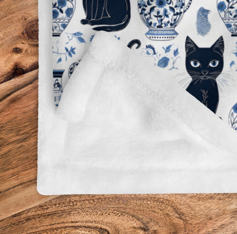 K&ouml;nnte beinhalten: Wei&szlig;e Fleece-Decke mit einem sich wiederholenden Muster aus schwarzen Katzen und blau-wei&szlig;en Porzellanvasen. Das Muster erinnert an traditionelles chinesisches Blau-Wei&szlig;-Porzellan.