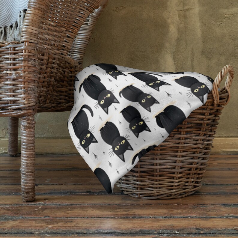 May include: A white throw blanket with a black cat pattern. The blanket is folded and placed in a wicker basket.