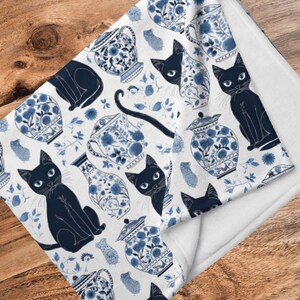 K&ouml;nnte beinhalten: Wei&szlig;e Fleece-Decke mit einem blauen und wei&szlig;en Muster aus schwarzen Katzen und chinesischen Porzellanvasen. Das Muster wiederholt sich &uuml;ber die gesamte Decke.