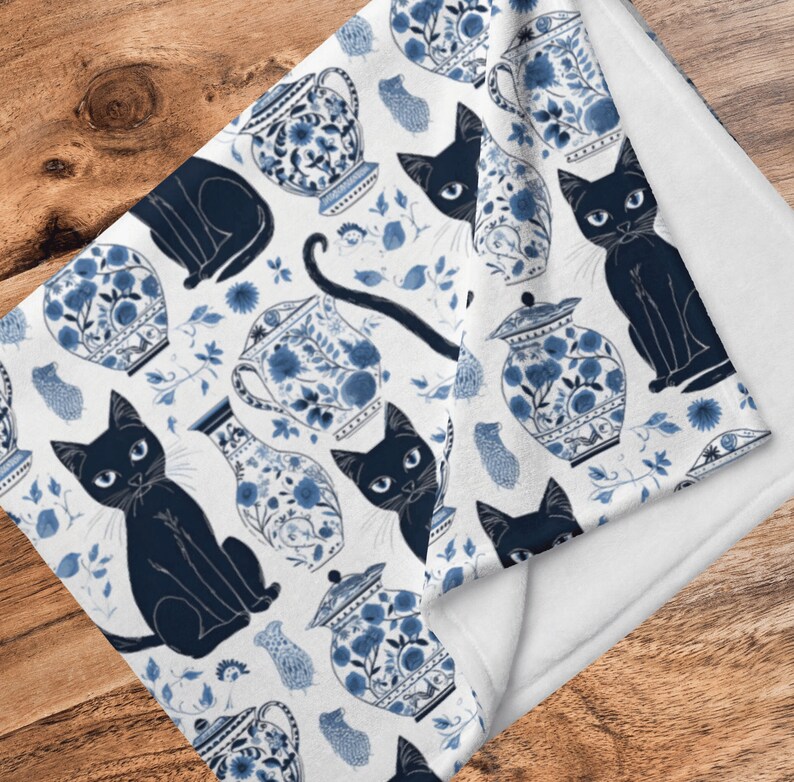 K&ouml;nnte beinhalten: Wei&szlig;e Fleece-Decke mit einem blauen und wei&szlig;en Muster aus schwarzen Katzen und chinesischen Porzellanvasen. Das Muster wiederholt sich &uuml;ber die gesamte Decke.