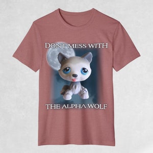 May include: A pink t-shirt with a cartoon wolf in front of a full moon. The text "DON'T MESS WITH THE ALPHA WOLF" is printed on the shirt.