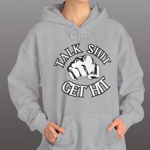 May include: A gray hoodie with a drawstring hood and front pocket. The hoodie features the text "TALK SHIT GET HIT" in a bold, stylized font, with a graphic of a clenched fist in the center. The design is in black and white.