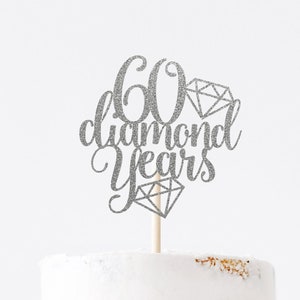 Silver cake topper with cursive writing saying '60 diamond years', with diamonds, pictured on a cake