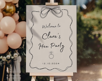 Pode incluir: Uma placa de boas-vindas retangular num cavalete de madeira com um desenho de linha preta de um laço no topo e um anel de diamante na parte inferior. O texto diz Welcome to Clare's Hen Party e a data 12.10.2024 em fonte cursiva preta.
