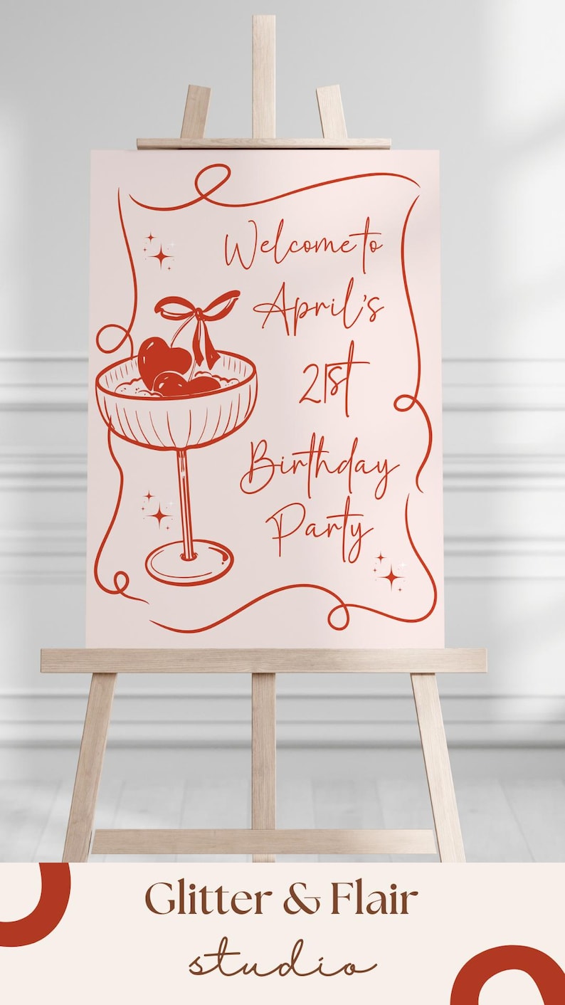 May include: A rectangular sign with a light pink background and red line art featuring a cocktail glass with cherries and a heart. The text reads: Welcome to April's 21st Birthday Party. The sign is displayed on a wooden easel with a studio logo below.