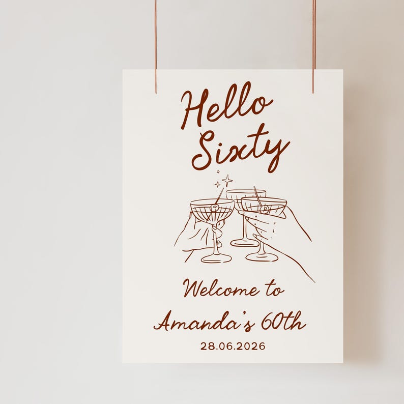 May include: A white rectangular sign with dark brown text and line art. The text reads Hello Sixty, Welcome to Amanda's 60th, and 28.06.2026. The illustration features three martini glasses being toasted, with a small star icon above them.