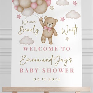 K&ouml;nnte beinhalten: Ein wei&szlig;es Babyparty-Schild mit einem Teddyb&auml;ren, der rosa und braune Ballons h&auml;lt. Auf dem Schild steht "We can Bearly Wait! Welcome to Emma and Jay's Baby Shower 02.11.2024"
