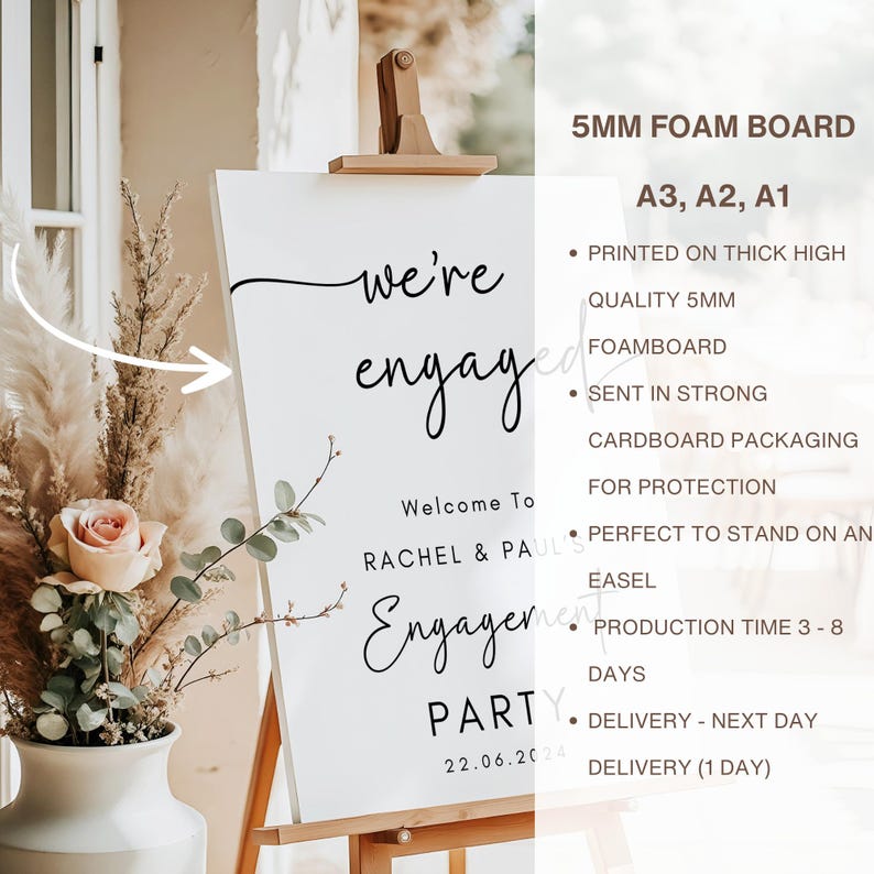 May include: A white 5mm foam board sign on a wooden easel featuring black text that reads we're engaged, Welcome To, RACHEL & PAUL'S Engagement PARTY, and the date 22.06.2024. The sign is displayed next to a vase containing dried pampas grass and roses.