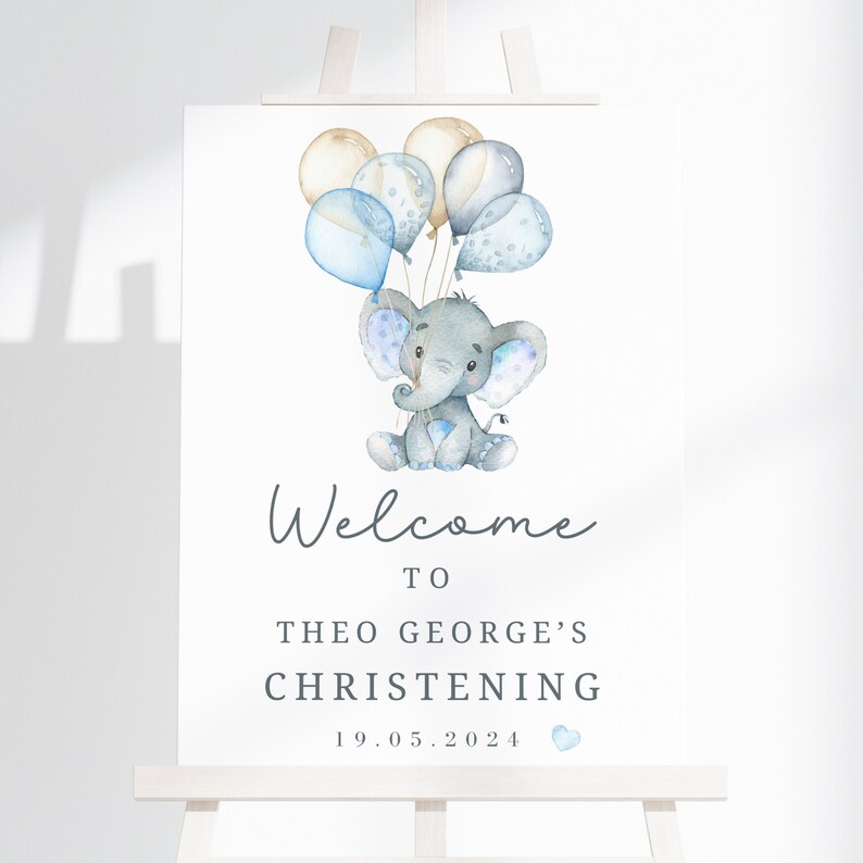 Pode incluir: Uma placa retangular branca com uma ilustra&ccedil;&atilde;o em aquarela de um elefante cinza segurando bal&otilde;es azuis e bege. O texto diz Welcome to Theo George's Christening 19.05.2024 com um pequeno &iacute;cone de cora&ccedil;&atilde;o azul abaixo da data.