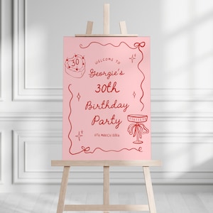 K&ouml;nnte beinhalten: Ein rosa Schild auf einer Holzstaffelei mit rotem Text und Illustrationen. Es verk&uuml;ndet "Willkommen zu Georgies 30. Geburtstagsparty" mit einem Kuchen und Tisch. Das Datum ist der "7. M&auml;rz 2026".