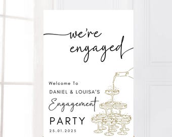 May include: White sign with black text that reads "we're engaged" and "Welcome to Daniel & Louisa's Engagement Party 25.01.2025". The sign also features a gold illustration of champagne glasses with a bottle pouring champagne into the top glass.