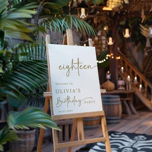 May include: A white welcome sign with gold lettering on an easel. The sign reads "eighteen" and "Welcome to Olivia's Birthday Party 09.03.2024".
