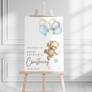 May include: Welcome to D&aacute;ire Patrick's Christening sign with a teddy bear holding blue and beige balloons and stars. The date 10.09.2023 is printed below the text.