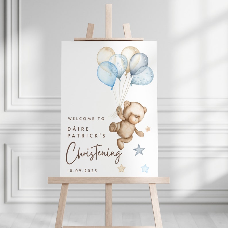 May include: Welcome to D&aacute;ire Patrick's Christening sign with a teddy bear holding blue and beige balloons and stars. The date 10.09.2023 is printed below the text.
