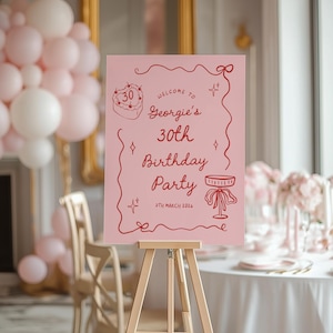 K&ouml;nnte beinhalten: Ein rosa Schild auf einer Holzstaffelei mit roter Schrift, das "Georgies 30. Geburtstagsparty" ank&uuml;ndigt. Der Text enth&auml;lt Illustrationen von Kuchen und Tisch. Der Hintergrund zeigt rosa und wei&szlig;e Ballons.