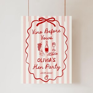 May include: A vertical sign with a pink and white striped background. The sign features a red decorative border and text that reads "Vino Before Vows" and "Olivia's Hen Party". The sign also includes illustrations of grapes, a wine bottle, a wine glass, cheese, and bread.