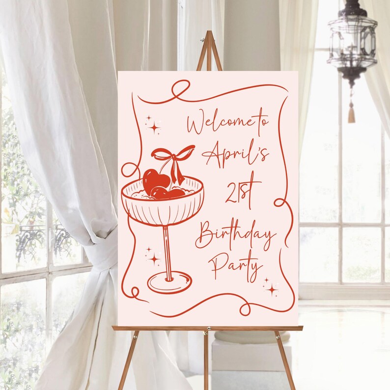 May include: A rectangular sign on a wooden easel featuring a light pink background with red line art. The design includes a cocktail glass with cherries and the text: Welcome to April's 21st Birthday Party, framed by decorative red swirls.