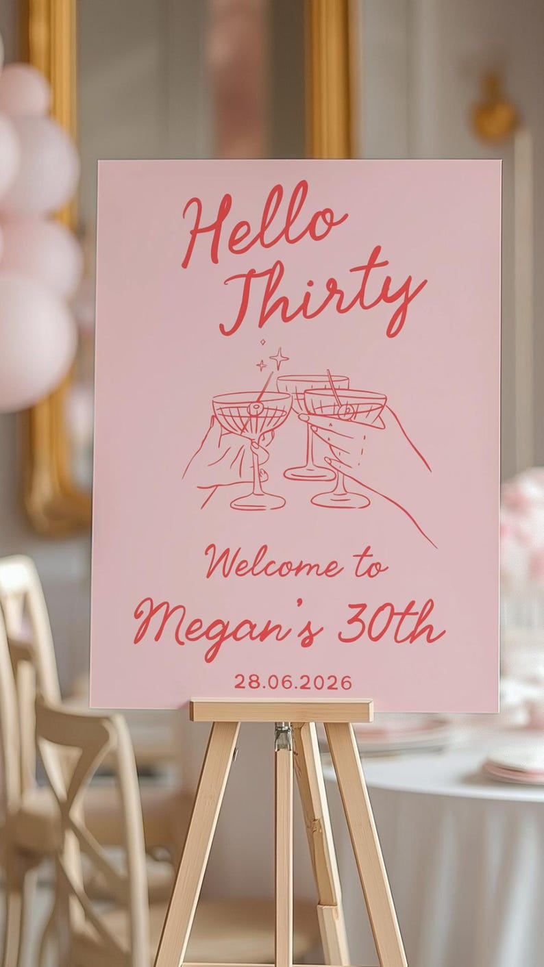May include: A rectangular pink sign featuring red text that reads Hello Thirty, Welcome to Megan's 30th, and 28.06.2026. The center graphic displays red line art of two hands holding martini glasses in a toast, accented by small star symbols.