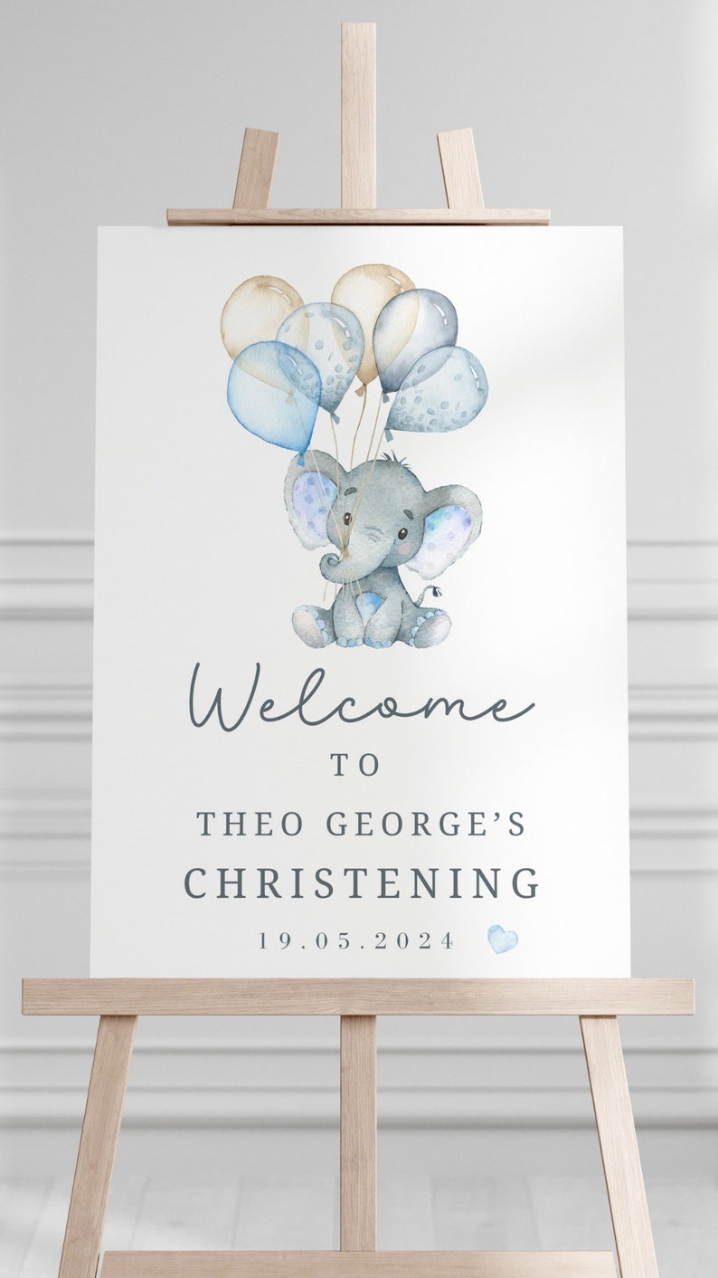 Pode incluir: Uma placa retangular branca com uma ilustra&ccedil;&atilde;o em aguarela de um elefante cinzento a segurar bal&otilde;es azuis e beges. O texto diz Welcome TO THEO GEORGE'S CHRISTENING 19.05.2024 com um pequeno &iacute;cone de cora&ccedil;&atilde;o azul junto &agrave; data.