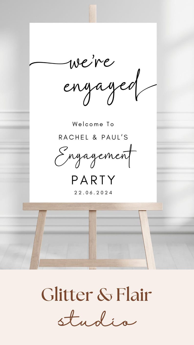 May include: A white rectangular sign on a wooden easel featuring black text that reads we're engaged, Welcome To RACHEL & PAUL'S Engagement PARTY, and the date 22.06.2024. The sign uses a combination of cursive and sans-serif typography.