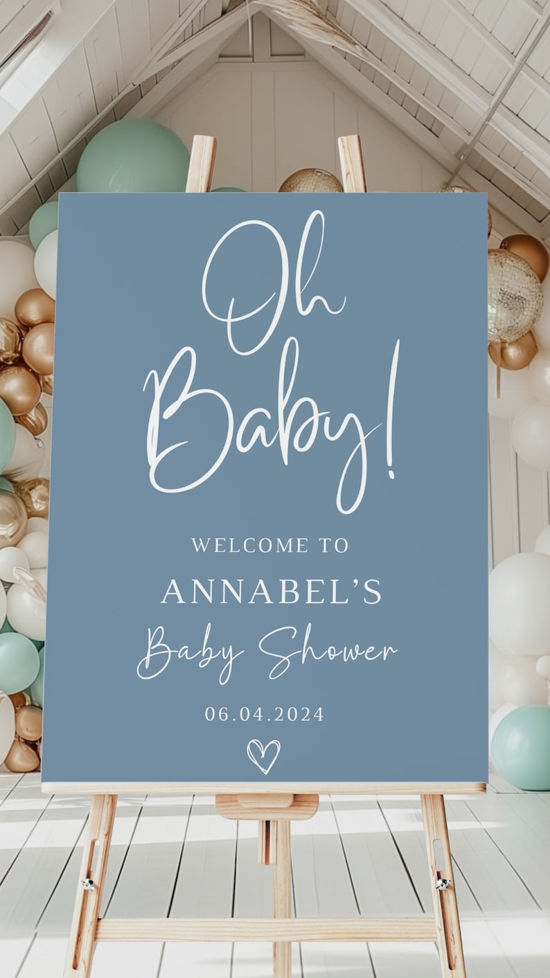 May include: A rectangular blue welcome sign for a baby shower featuring white text that reads Oh Baby! WELCOME TO ANNABEL'S Baby Shower 06.04.2024 with a small heart icon at the bottom, displayed on a light-colored wooden easel stand.