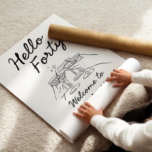 May include: A white poster featuring black line art of two hands holding martini glasses with olives. The text reads Hello Forty and Welcome to. The poster is partially rolled up, with a brown cardboard shipping tube resting on the top edge.