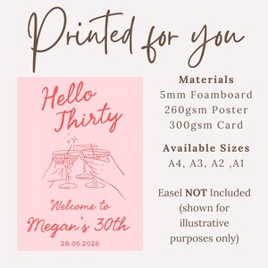 May include: A pink rectangular sign with the text Printed for you, Hello Thirty, Welcome to Megan's 30th, and 28.06.2026. It features a line drawing of hands holding cocktail glasses. Material options include 5mm foamboard, 260gsm poster, and 300gsm card.