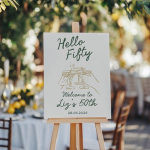 May include: A white rectangular sign on a wooden easel featuring dark green text that reads Hello Fifty, Welcome to Liz's 50th, and the date 28.06.2026. The center graphic shows gold line art of three hands holding cocktail glasses with a small star.