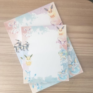 May include: Two sheets of stationery featuring watercolor illustrations of various cartoon creatures. The stationery has a white background with pastel watercolor accents in blue, pink, and purple. The cartoon creatures are in various poses around the edges.