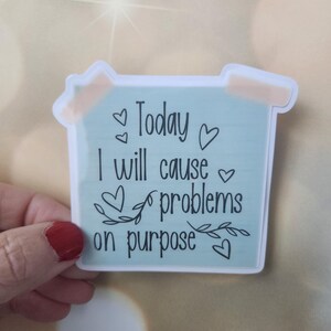 May include: A light blue sticker with the text "Today I will cause problems on purpose" with hearts and leaves around the text.