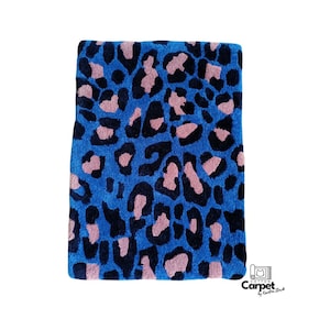 Op de afbeelding: Blauw en roze luipaardprint tapijt. Het tapijt is gemaakt van een zacht, pluche materiaal en heeft een modern ontwerp.